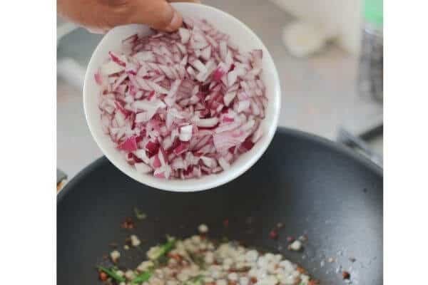 Onion being added to the spluttering seeds and oil